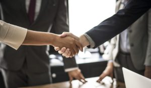 Two professionals shaking hands in front of other professionals.